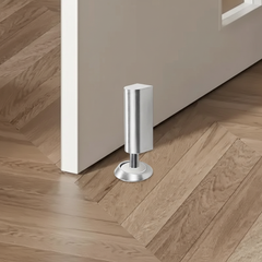 Silver magnetic floor door stop beside a door on wood flooring