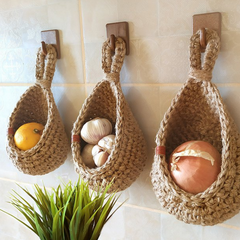 Three hanging cotton-yarn wall baskets holding household produce