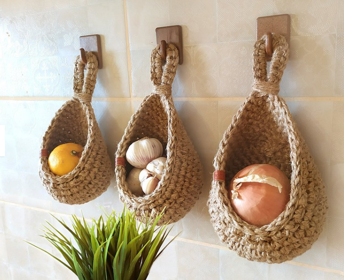 Three hanging cotton-yarn wall baskets holding household produce