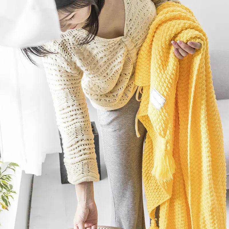 Yellow knitted tassel throw held beside a neutral throw